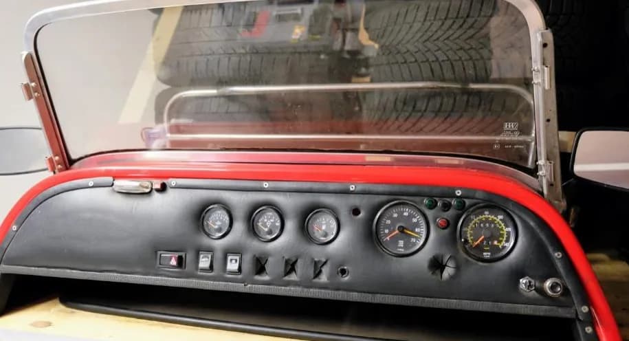 Dashboard compleet met analoge klokken (temp, oliedruk, laadstroom, toerenteller, snelheidsmeter) en rood-omrande windscreen-frame.