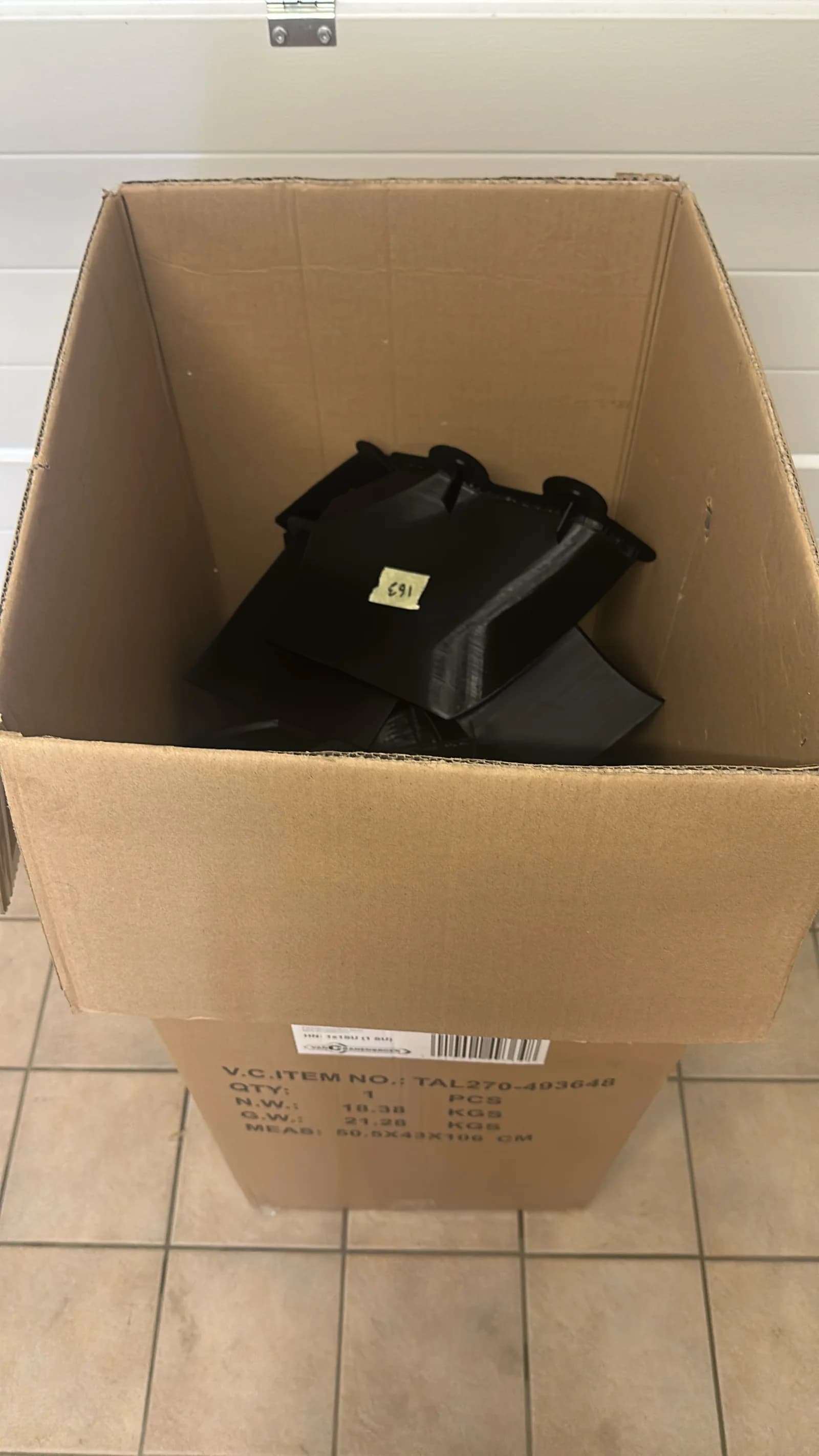 Grote kartonnen doos gevuld met stapels vers-geprinte zwarte body-stukken, klaar om te worden gesorteerd en aan elkaar gesmolten.