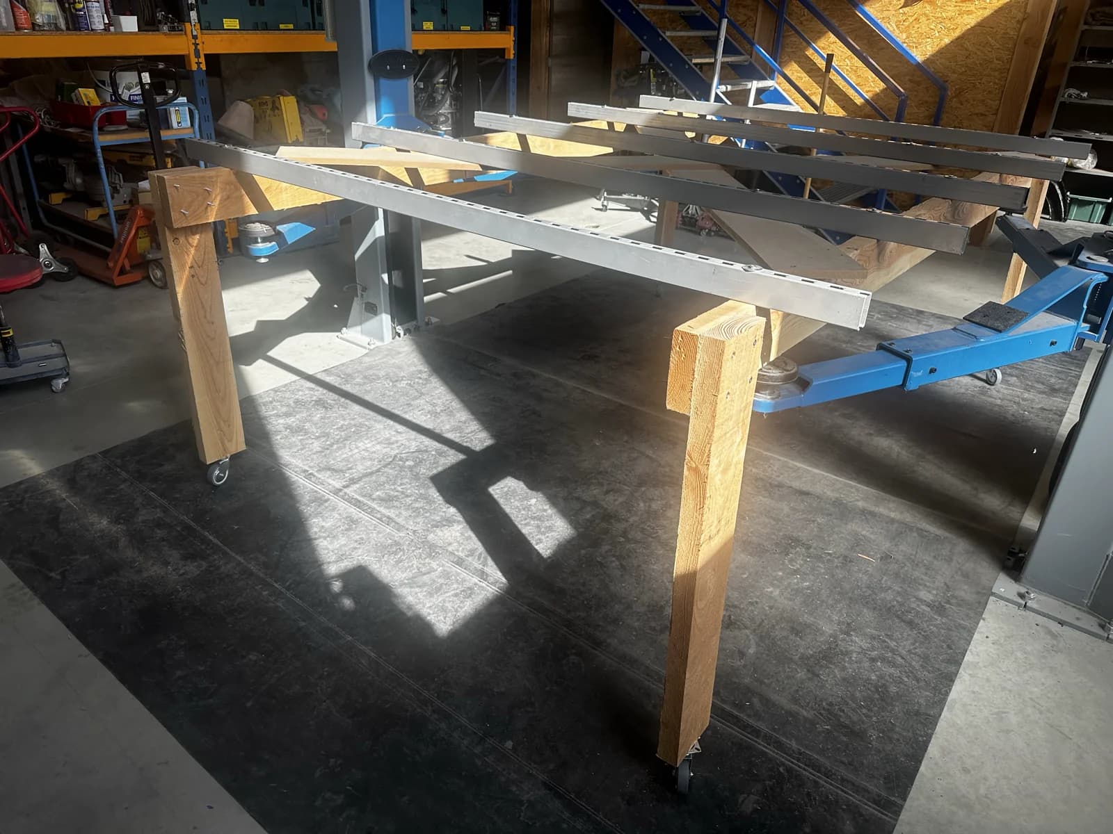 Zelfgebouwde rek-structuur van houten balken en stalen U-profielen op wielen, op de vloer van het atelier — klaar om de body aan op te hangen.
