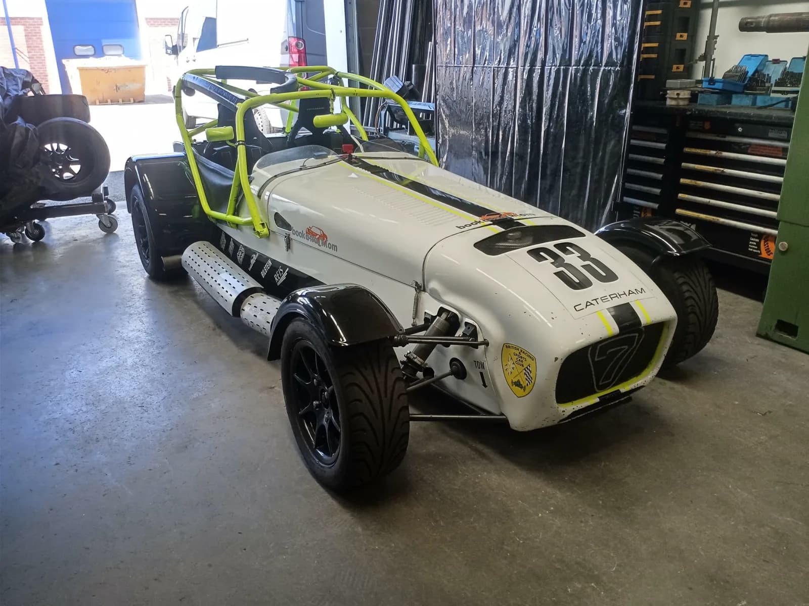 Dans Caterham in de garagebox voor Castle Combe. Wit met gele rolbeugel, race-nummer 33 op de neus.